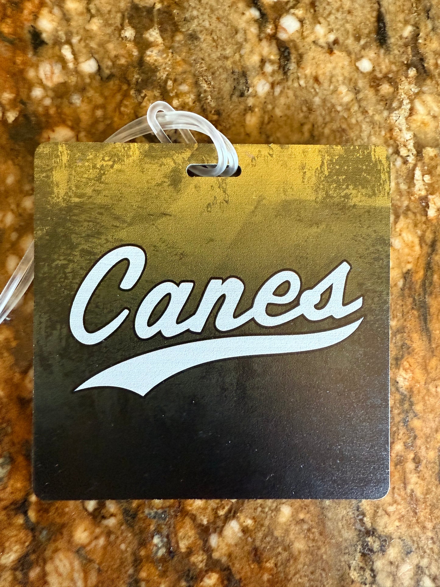Gold and black tag with 'Canes' logo on a textured surface