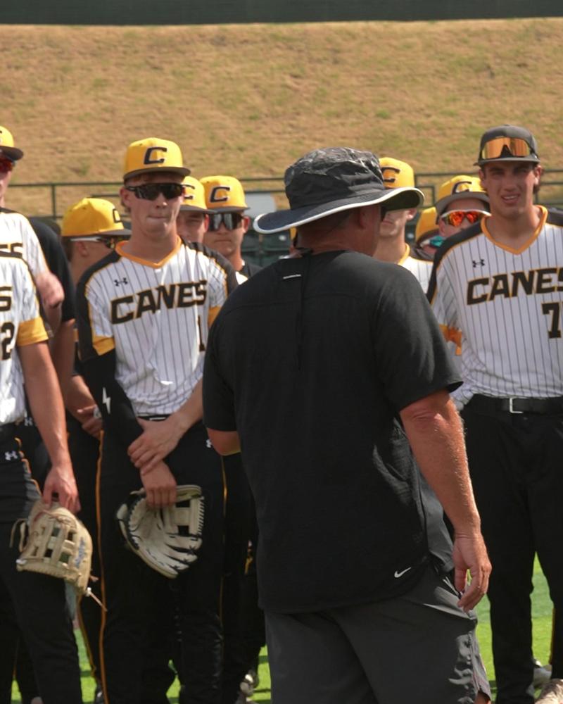 Canes players in black and gold gathered around their coach on the field